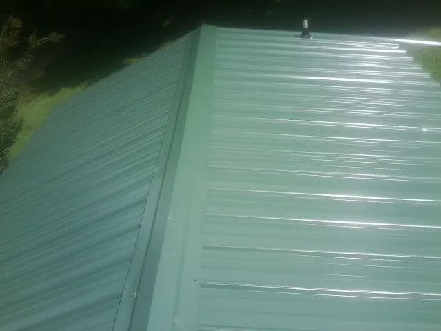 New green metal panels meeting at the ridge of a roof — Flat Roof Repair work by our crew in Newell