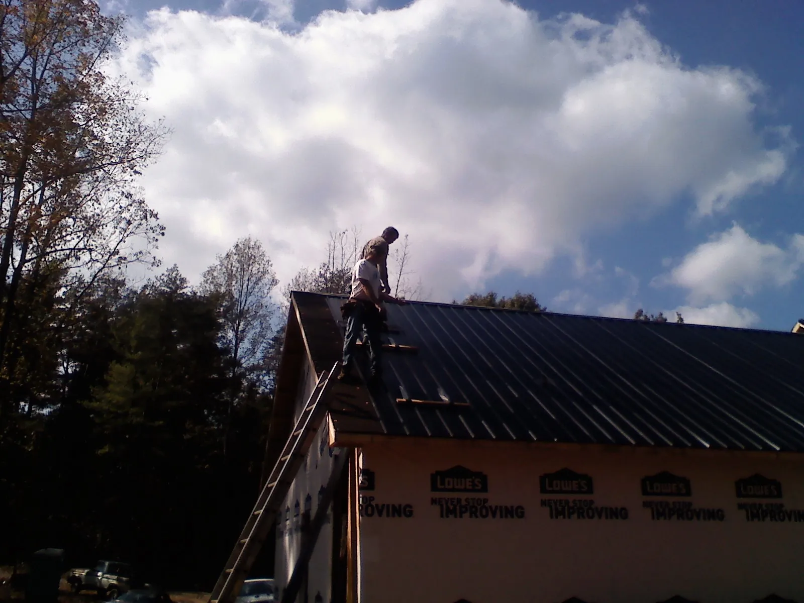 Roofer fastening dark metal panels high against a cloudy sky, from a Roof Inspection job in Newell